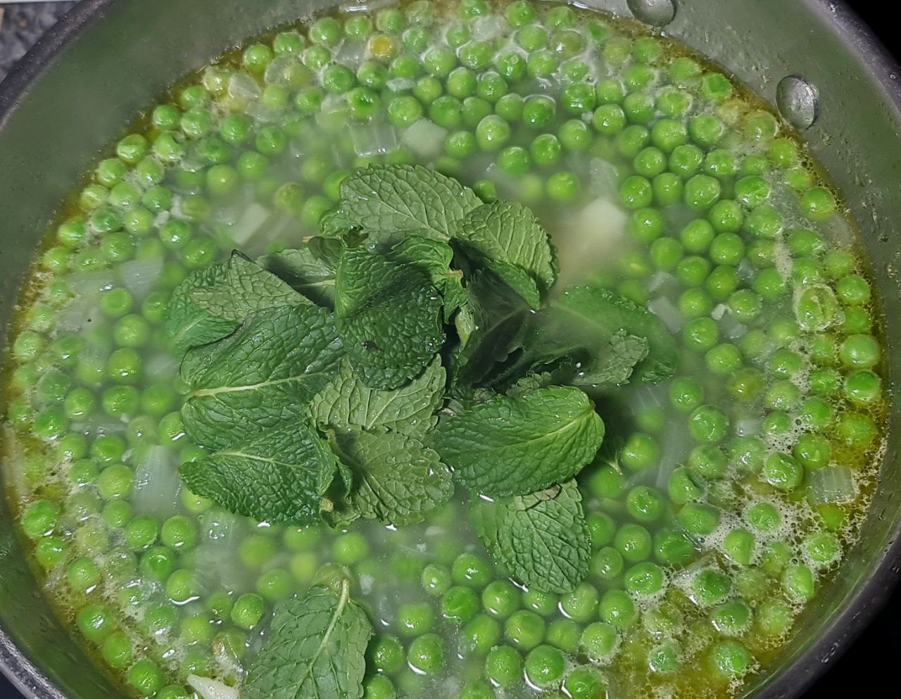 Fresh green peas simmering in a pot with mint leaves for a vibrant and refreshing pea and mint soup.