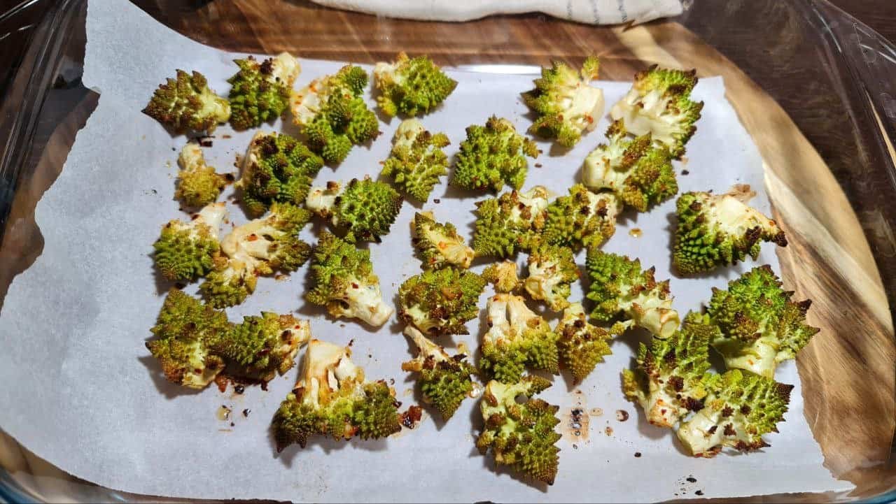 Roasted Romanesco florets on a parchment-lined baking sheet, showcasing their vibrant green color and unique fractal pattern.