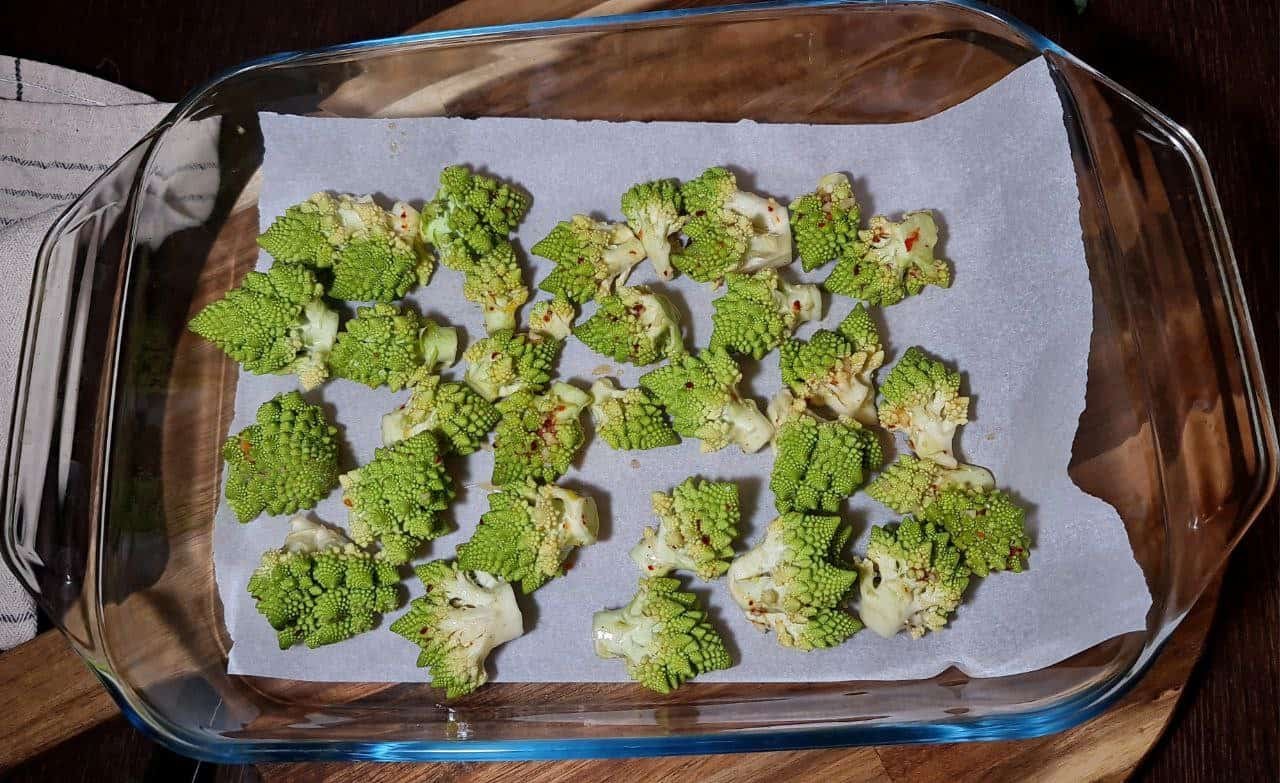 Chopped Romanesco florets seasoned and arranged on a parchment-lined baking dish, ready for roasting.