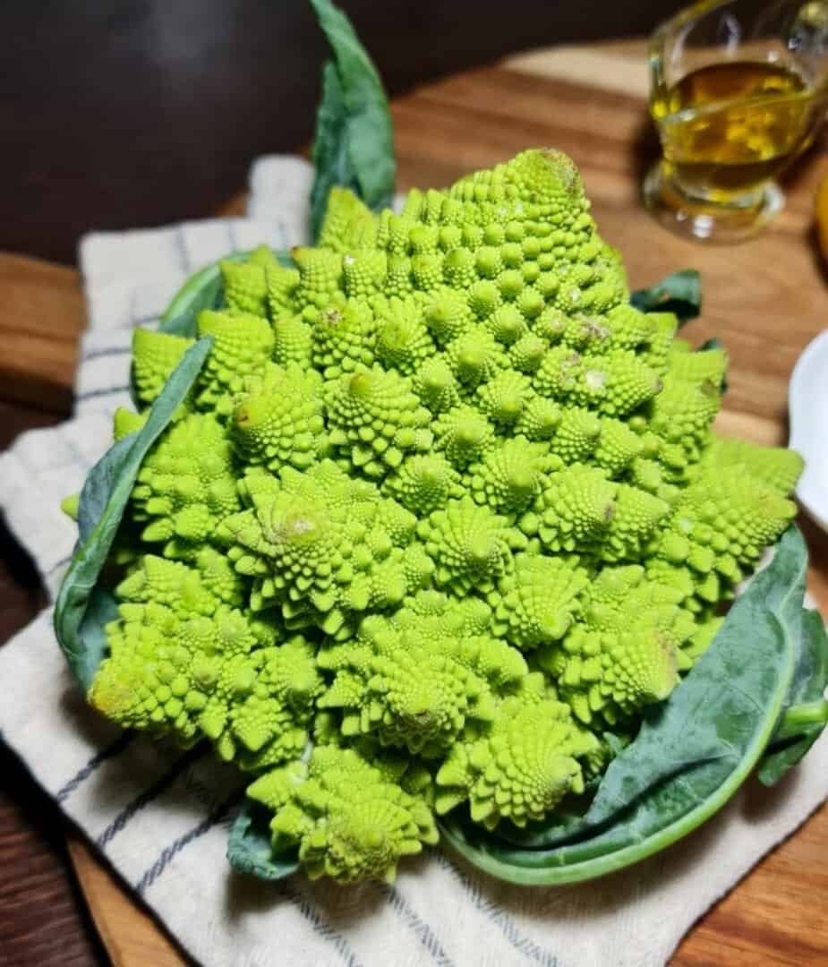 Fresh Romanesco broccoli on a wooden cutting board with a small glass of olive oil in the background.