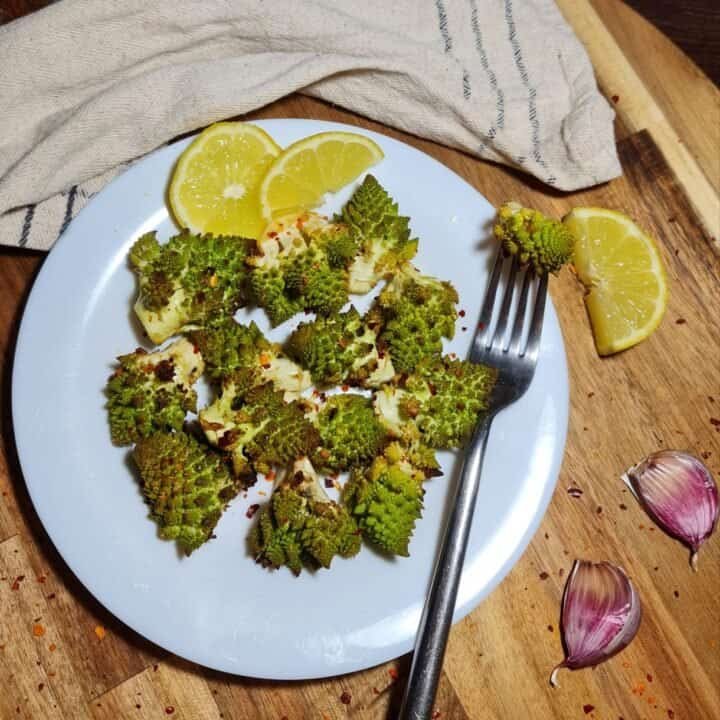 Plate of roasted Romanesco with lemon slices and garlic cloves on a wooden board.