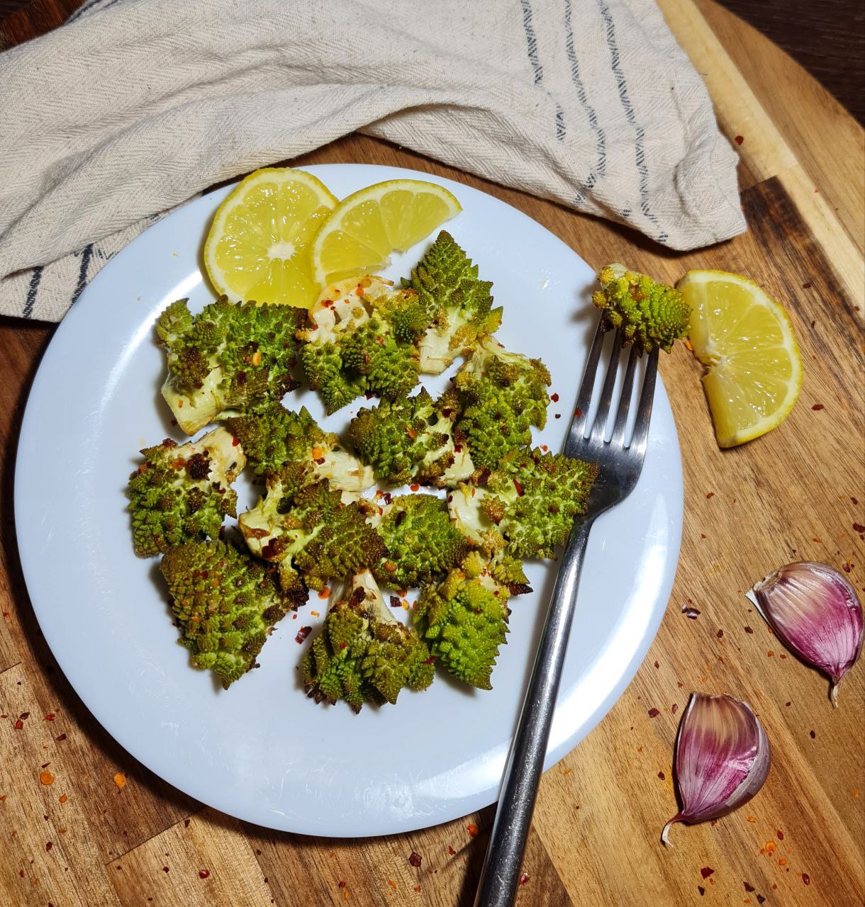 Plate of roasted Romanesco with lemon slices and garlic cloves on a wooden board.