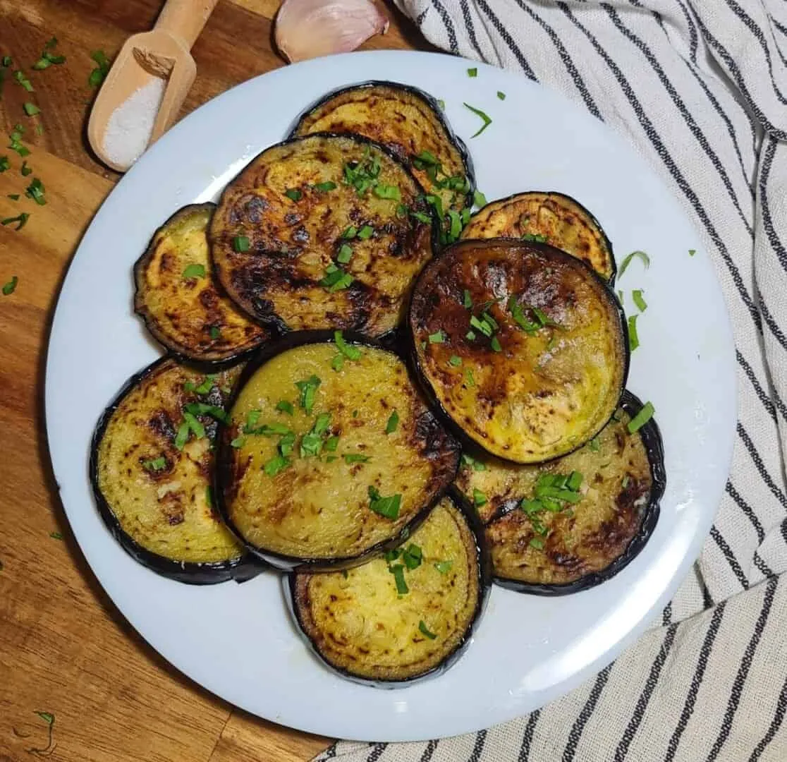 A plate of sauteed eggplant slices garnished with fresh herbs.