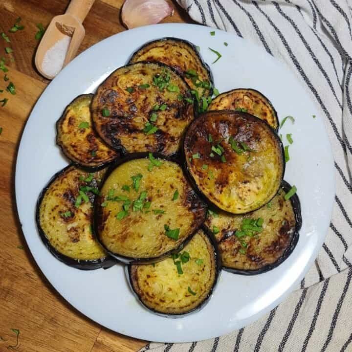 A plate of sauteed eggplant slices garnished with fresh herbs.