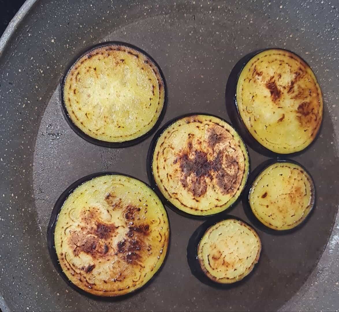  Slices of eggplant being sautéed in a pan until golden brown.