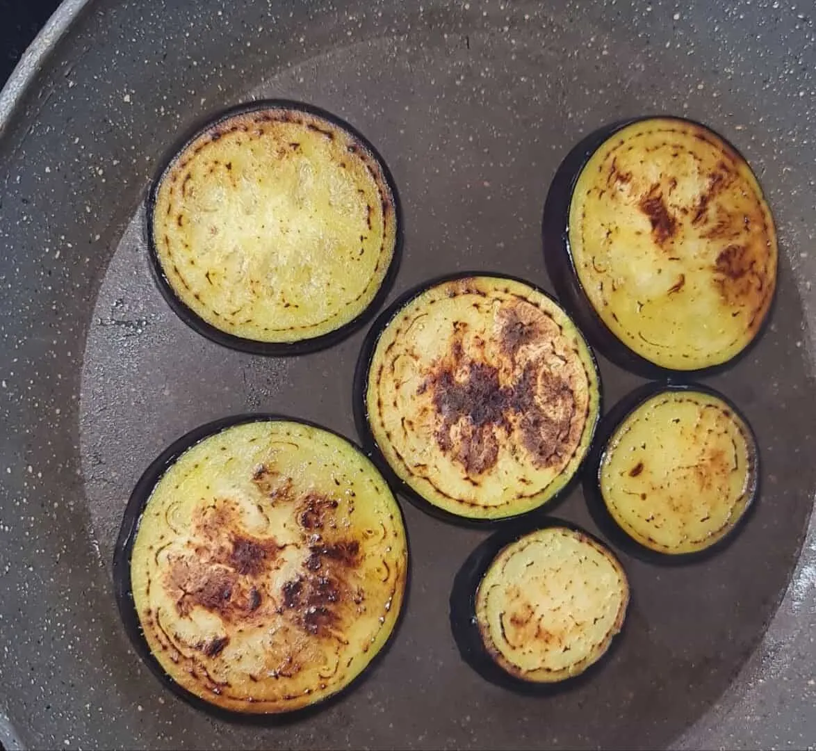  Slices of eggplant being sautéed in a pan until golden brown.