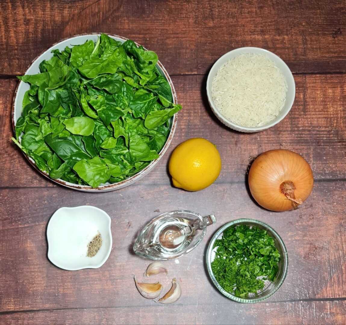 Ingredients for spinach rice including fresh spinach, garlic cloves, chopped herbs, and other ingredients on a wooden surface.