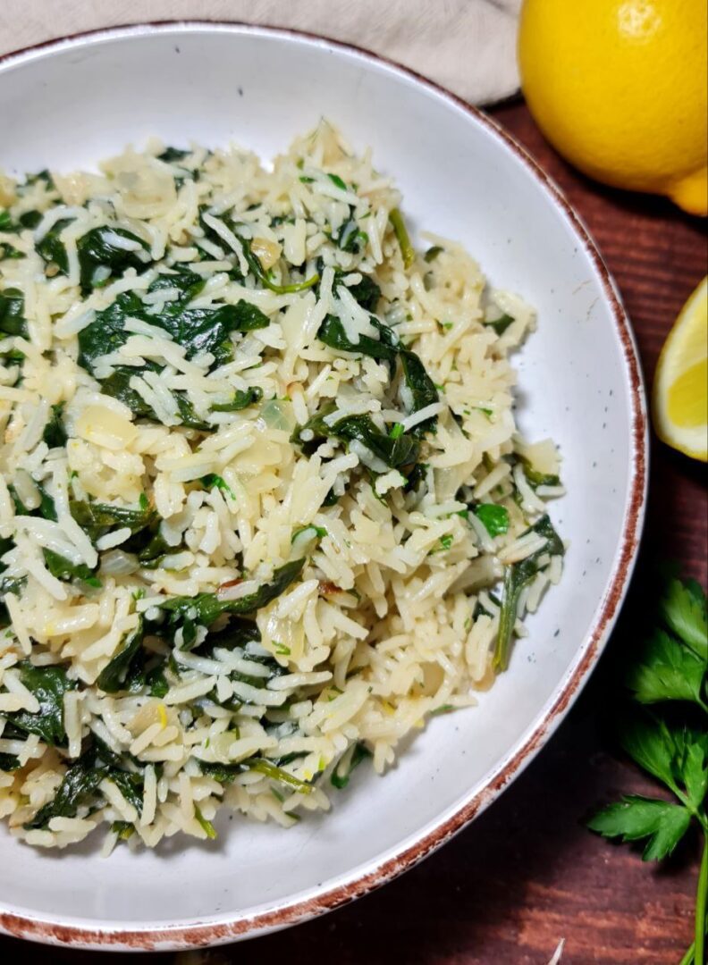 A close-up view of a bowl of spinach rice garnished with fresh herbs, with a lemon and parsley on the side.