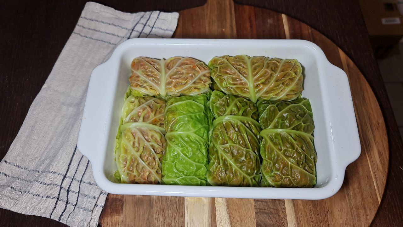 A white baking dish filled with neatly arranged vegan cabbage rolls, placed on a wooden cutting board with a cloth napkin underneath.