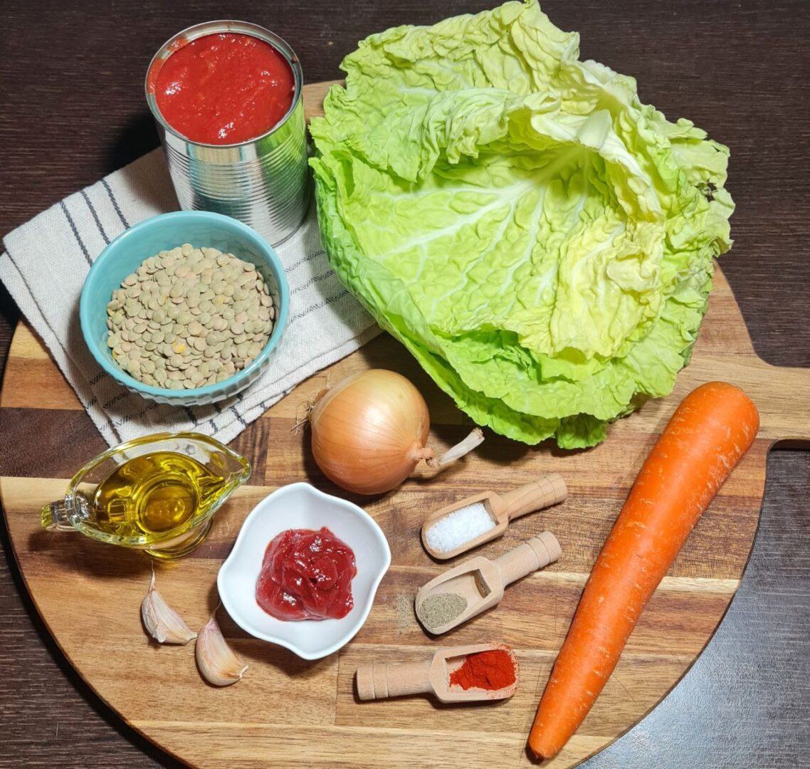 Ingredients for vegan cabbage rolls including cabbage, lentils, tomato paste, onion, carrot, garlic, olive oil, and spices.