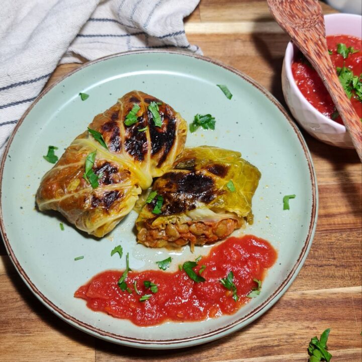 Vegan cabbage rolls served with tomato sauce and garnished with fresh parsley.