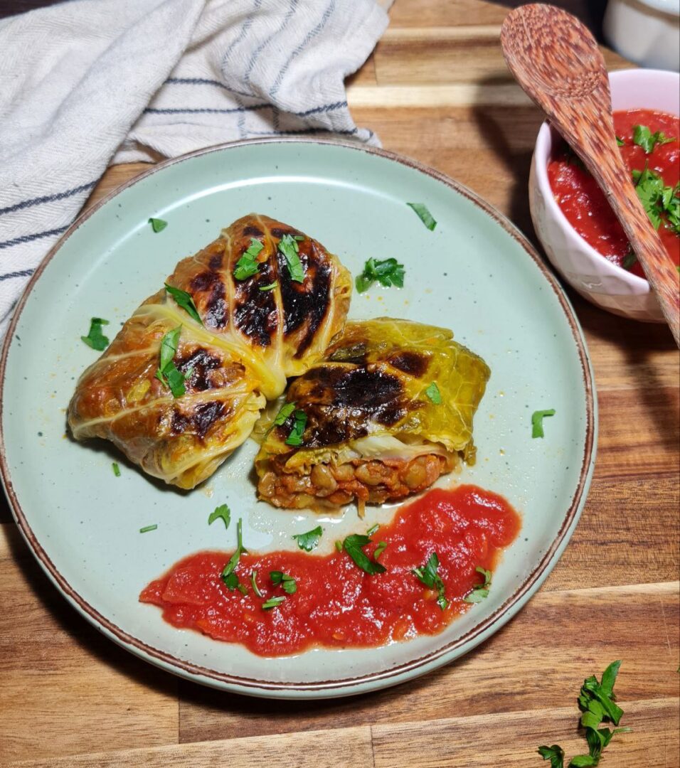 Vegan cabbage rolls served with tomato sauce and garnished with fresh parsley.