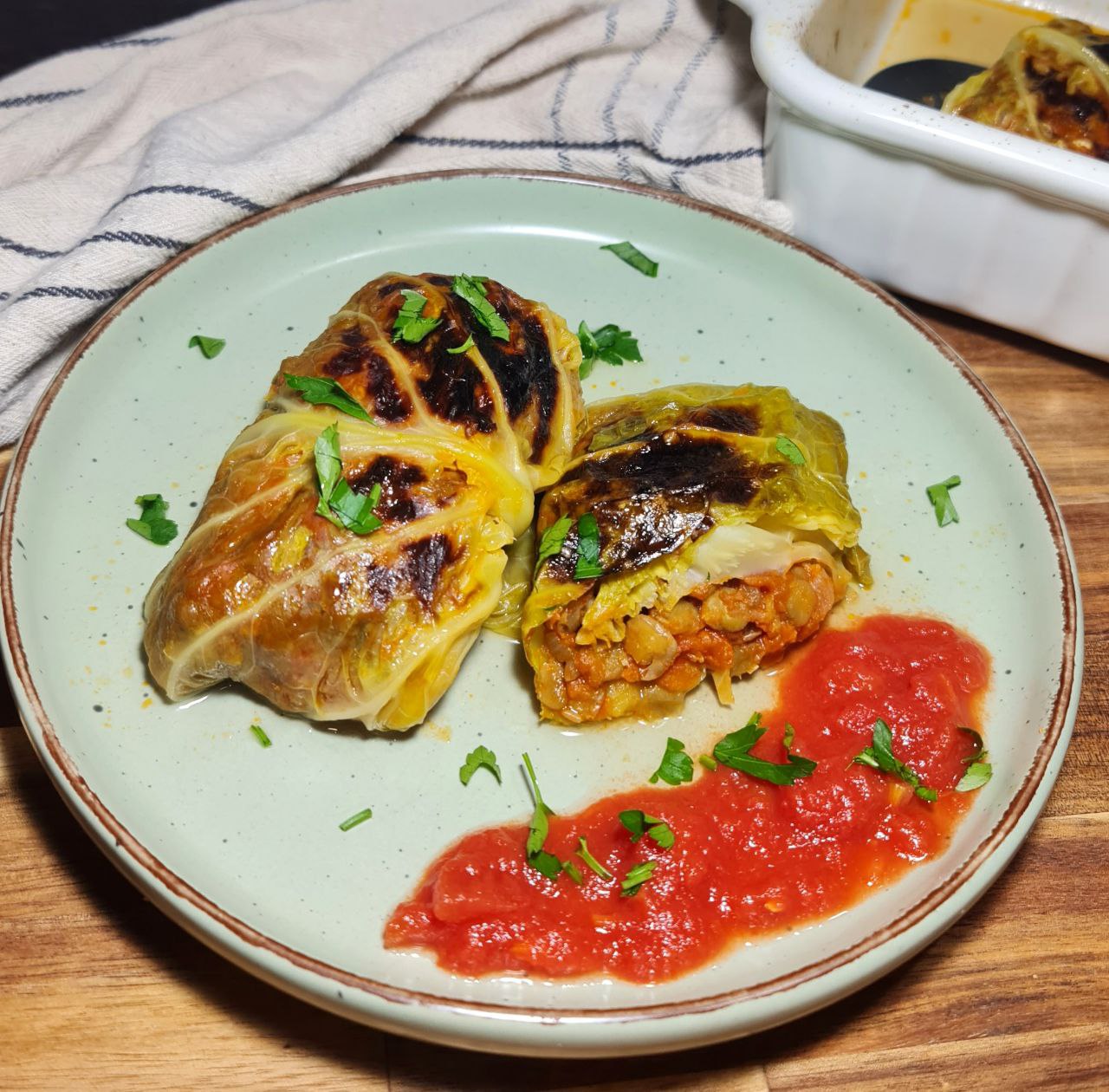 Two vegan cabbage rolls on a plate with tomato sauce and garnished with fresh herbs.