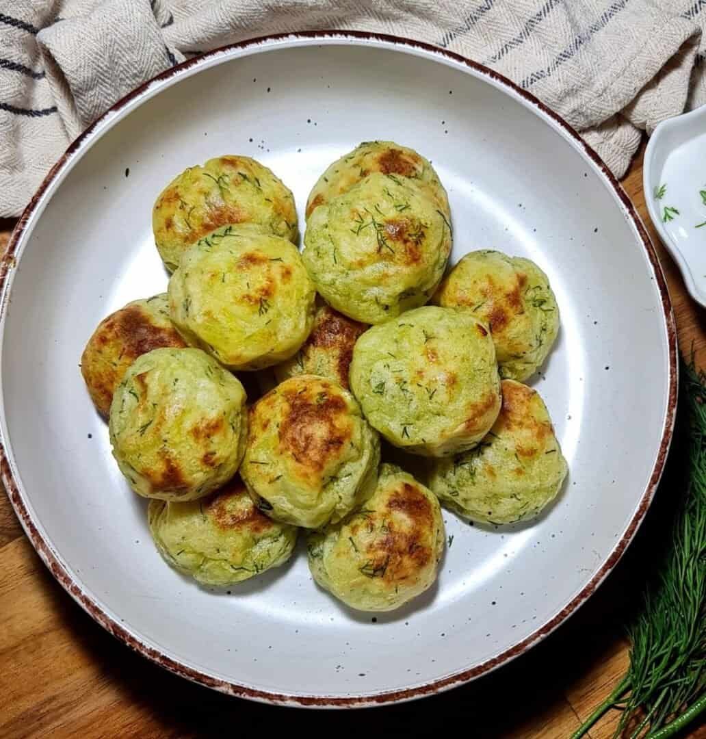 A plate of golden-brown vegan mashed potato balls garnished with fresh herbs.