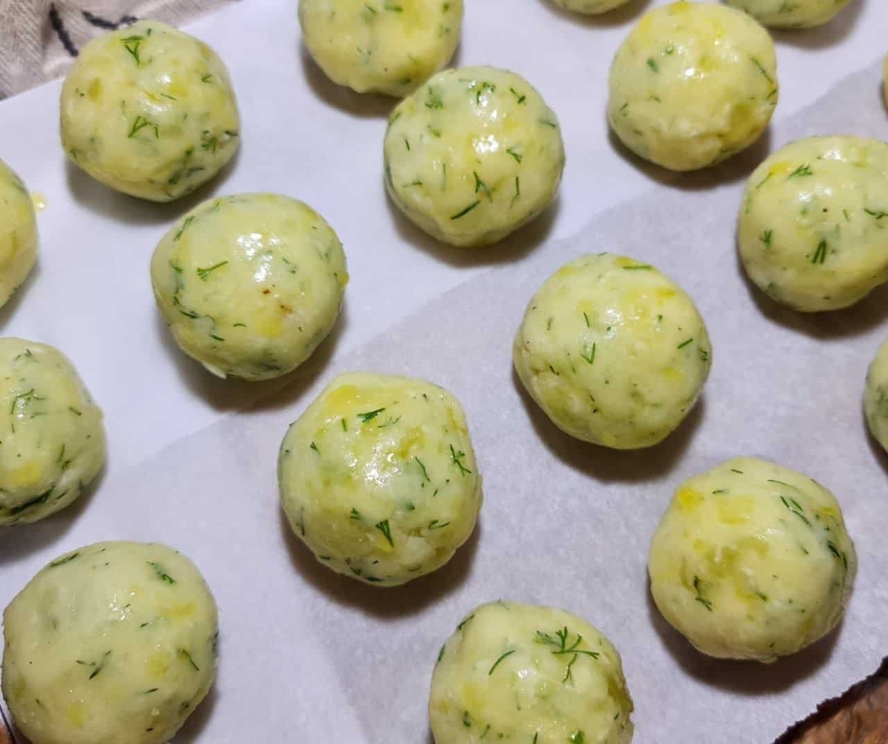  Vegan mashed potato balls with herbs on parchment paper.