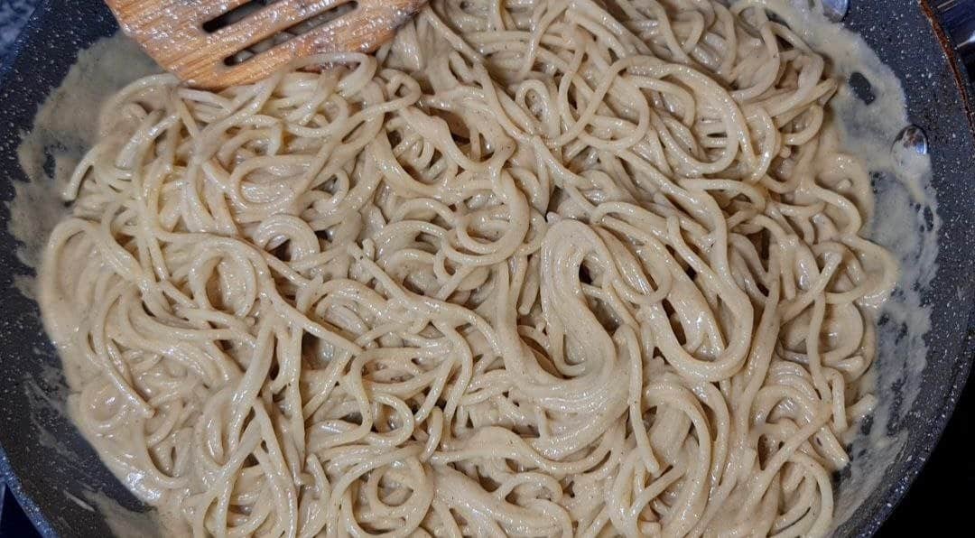 A pan of creamy vegan spaghetti alla Nerano with a wooden spatula.