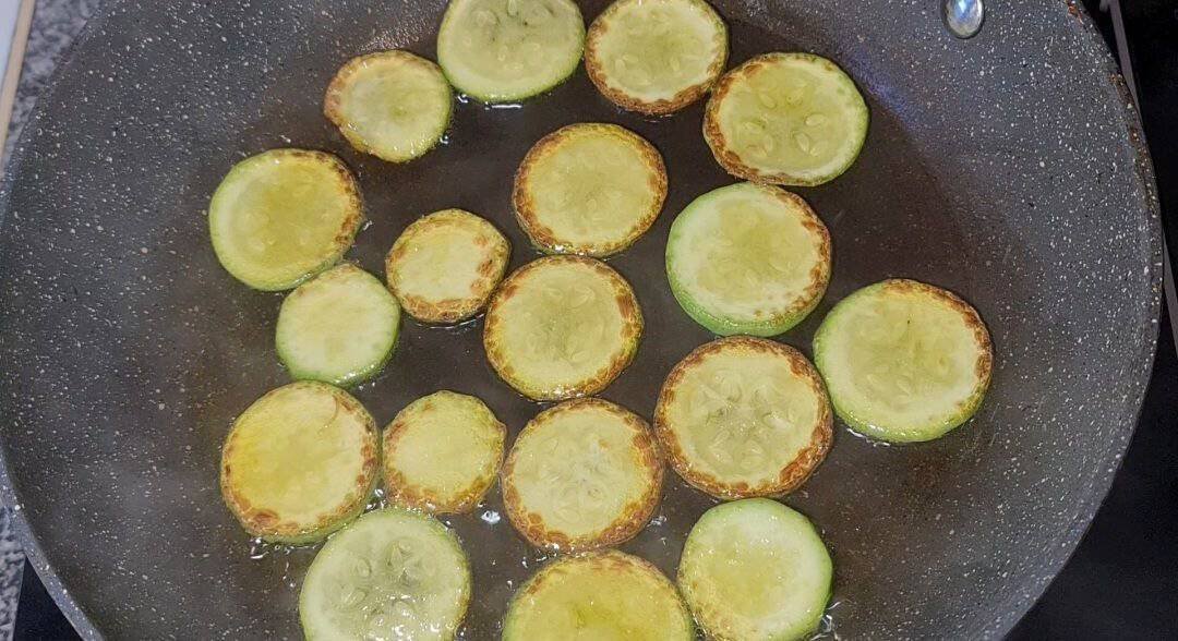 Sliced zucchini frying in a pan for vegan Spaghetti alla Nerano recipe.