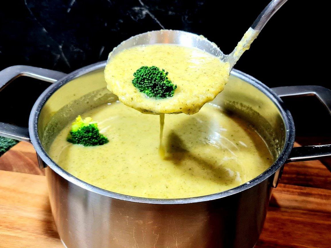 A ladle lifting creamy vegan broccoli soup with a broccoli floret from a pot.