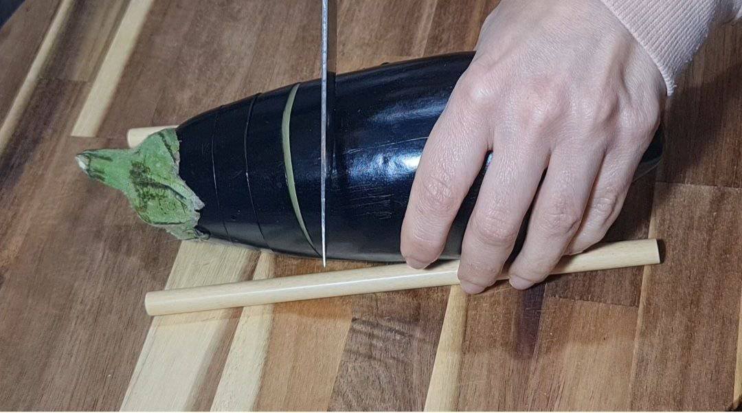 Slicing an eggplant with chopsticks on a wooden cutting board.