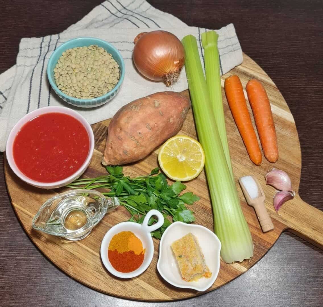 Ingredients for sweet potato lentil soup including sweet potato, lentils, carrots, celery, onion, garlic, parsley, lemon, tomato sauce, spices, vegetable broth cube, olive oil, and salt.