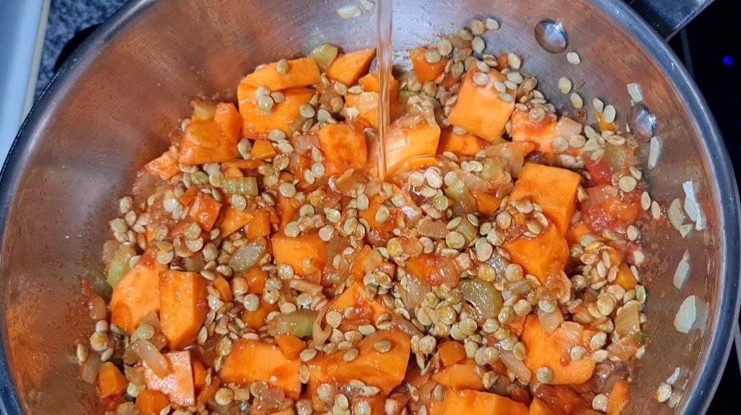 A pot filled with a mixture of sweet potatoes, lentils, onions, and other vegetables being cooked for sweet potato lentil soup.