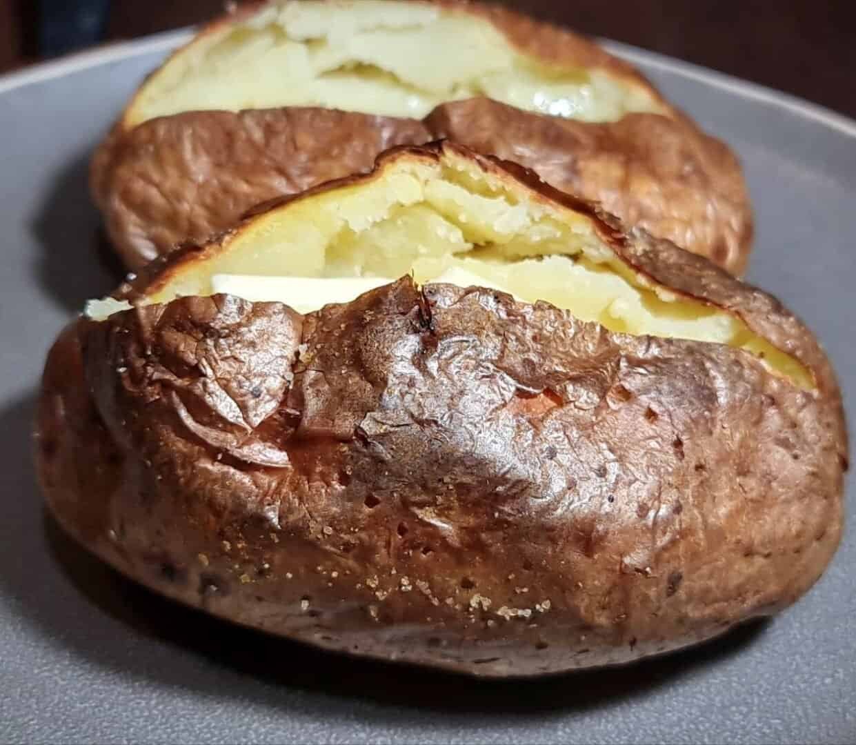 Close-up of two baked potatoes with crispy skin and fluffy interior on a gray plate.