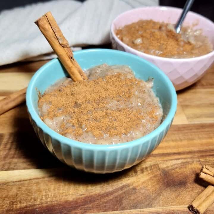 Two bowls of vegan rice pudding topped with cinnamon powder and a cinnamon stick.