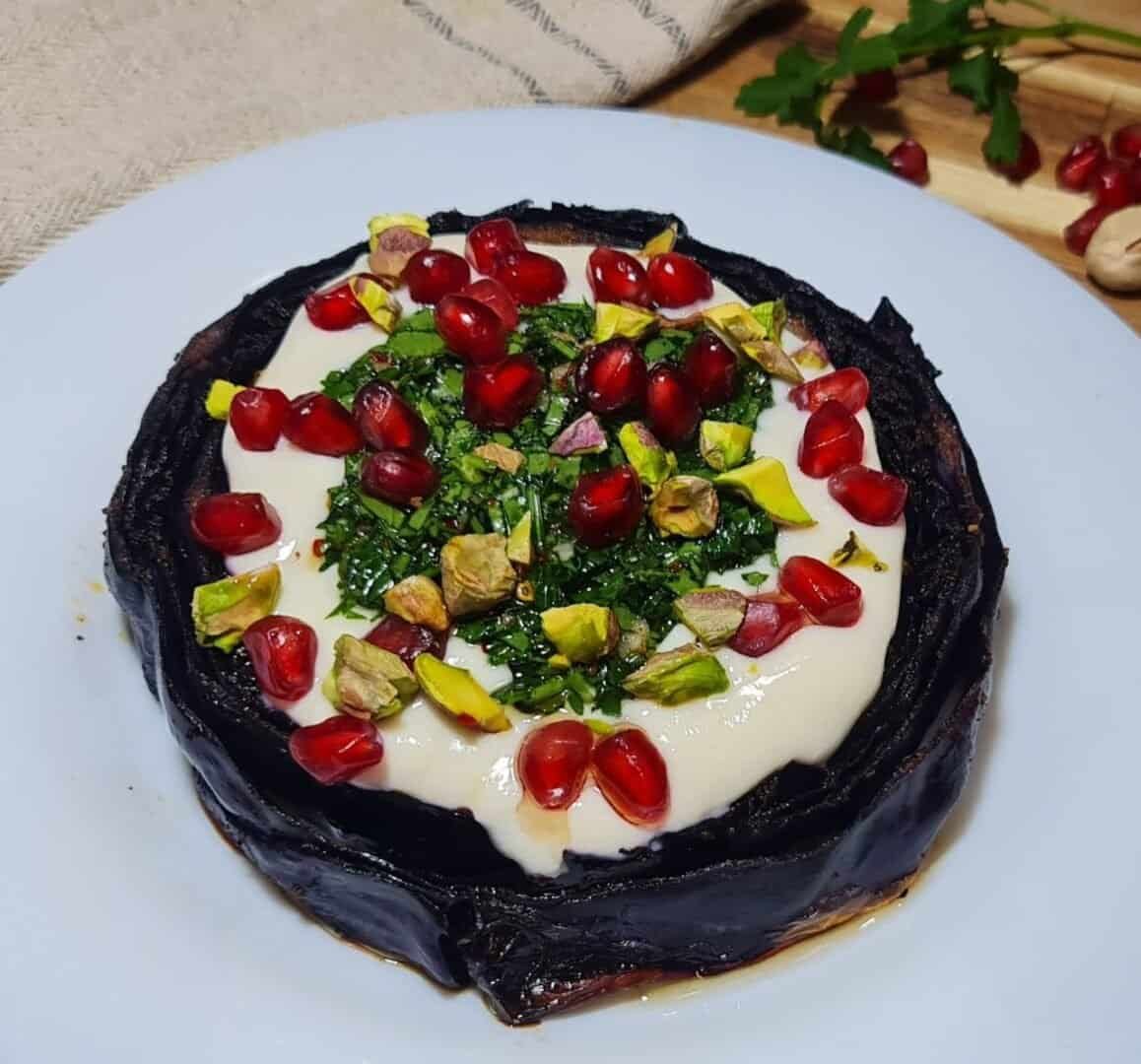 Vegan roasted cabbage steak topped with creamy sauce, pomegranate seeds, chopped herbs, and pistachios on a white plate.