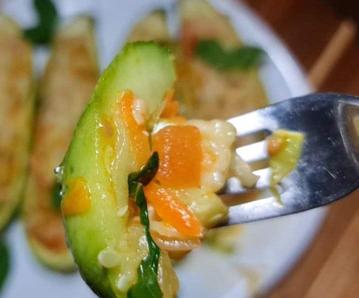 Close-up of a fork holding a piece of vegan stuffed zucchini with colorful vegetables.