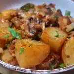 A bowl of Mediterranean Veggie Casserole, featuring cooked chunks of potatoes, mushrooms, zucchini, and other vegetables in a rich tomato-based sauce, garnished with fresh chopped herbs.