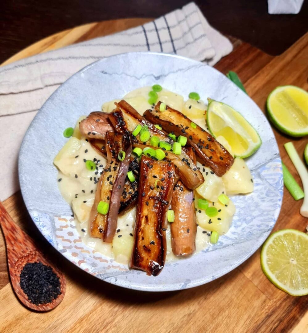 Angle shot of coconut potatoes crowned with soy-glazed Japanese eggplant, scallions, and sesame seeds. Coconut Potatoes Japanese Eggplant