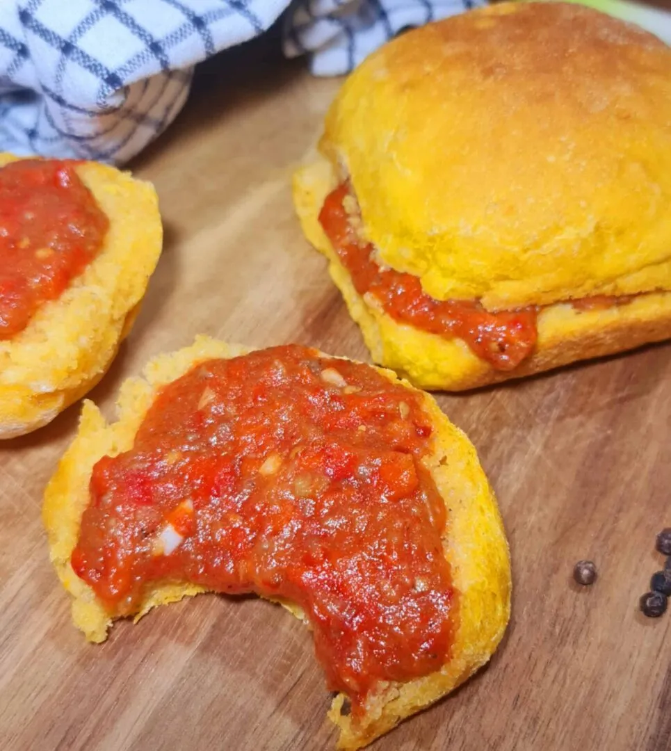 Half‑eaten Sweet Potato Dinner Roll topped with chunky tomato‑pepper sauce, showing airy crumb and bright filling.