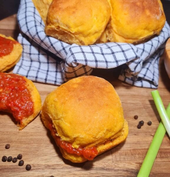 Golden Sweet Potato Dinner Roll layered with red pepper sauce on a wooden board next to peppercorns.