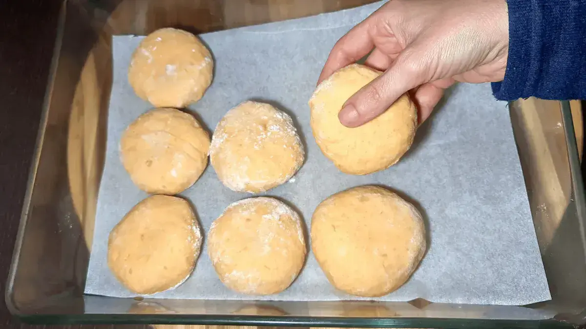 Hand placing a proofed Sweet Potato Dinner Roll dough ball into a parchment‑lined glass baking dish.