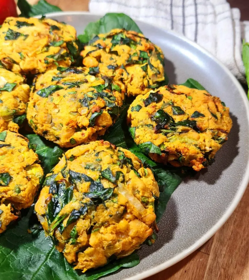 A plate of golden‑brown Vegan Chickpea Spinach Patties resting on fresh spinach leaves.