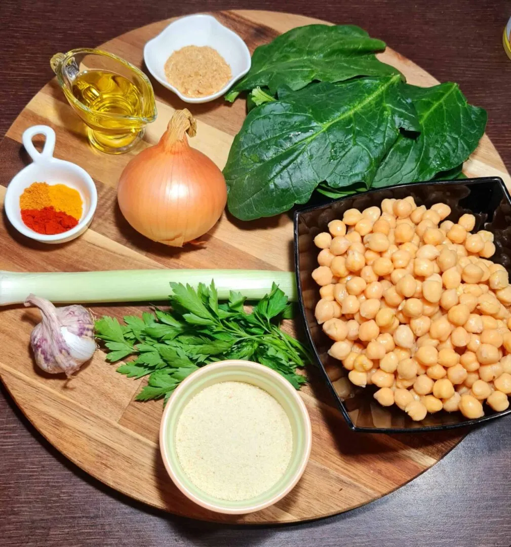Olive oil, spices, onion, garlic, celery, parsley, spinach leaves, chickpeas, and breadcrumbs arranged on a wooden board for Vegan Chickpea Spinach Patties.