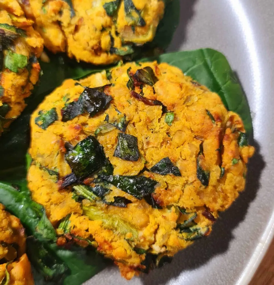 Vegan Chickpea Spinach Patties arranged on spinach leaves next to fresh tomatoes.