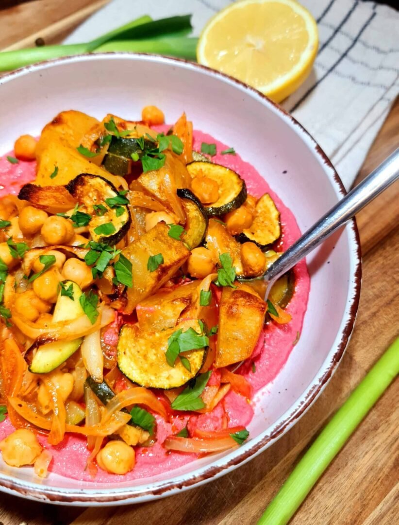 Angled shot of Vegan Roasted Veggie Bowl showing roasted vegetables over beet hummus with lemon half in background.