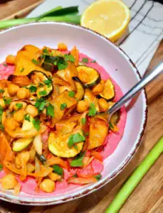 Angled shot of Vegan Roasted Veggie Bowl showing roasted vegetables over beet hummus with lemon half in background.