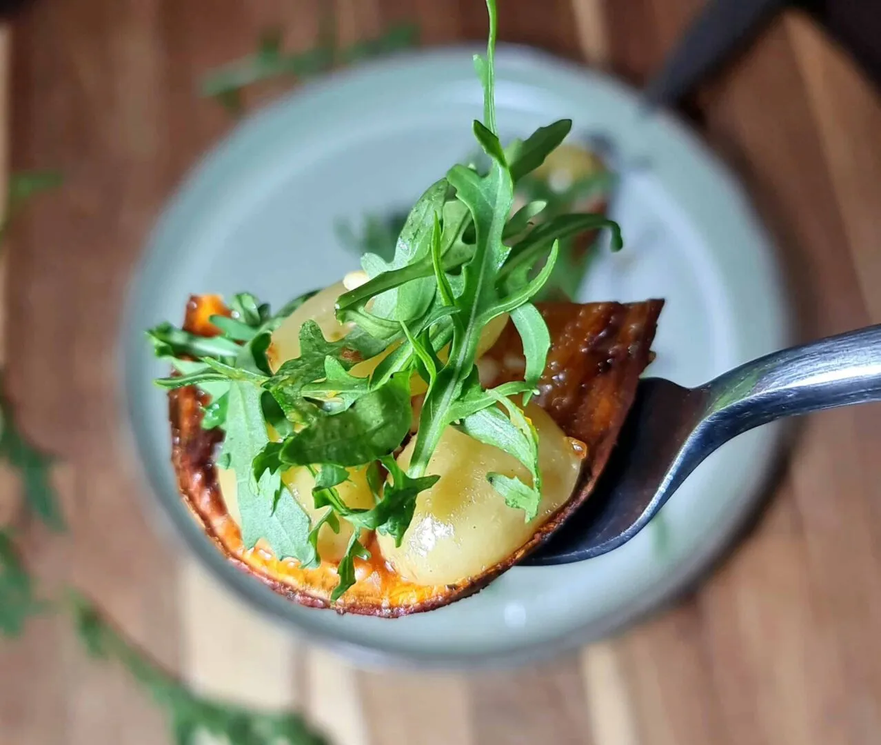 Fork holding bite of sweet potato toast against blurred plate background.