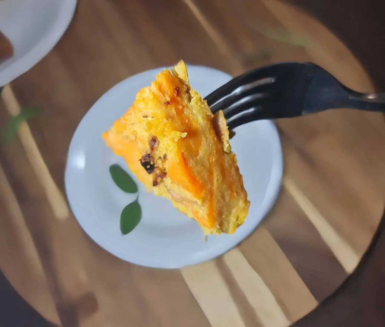 Fork holding a bite of golden sweet potato frittata over a blurred plate in the background.