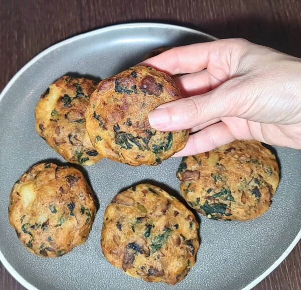 Hand holding Vegan Mushroom Potato Patty showing golden crust and spinach flecks.