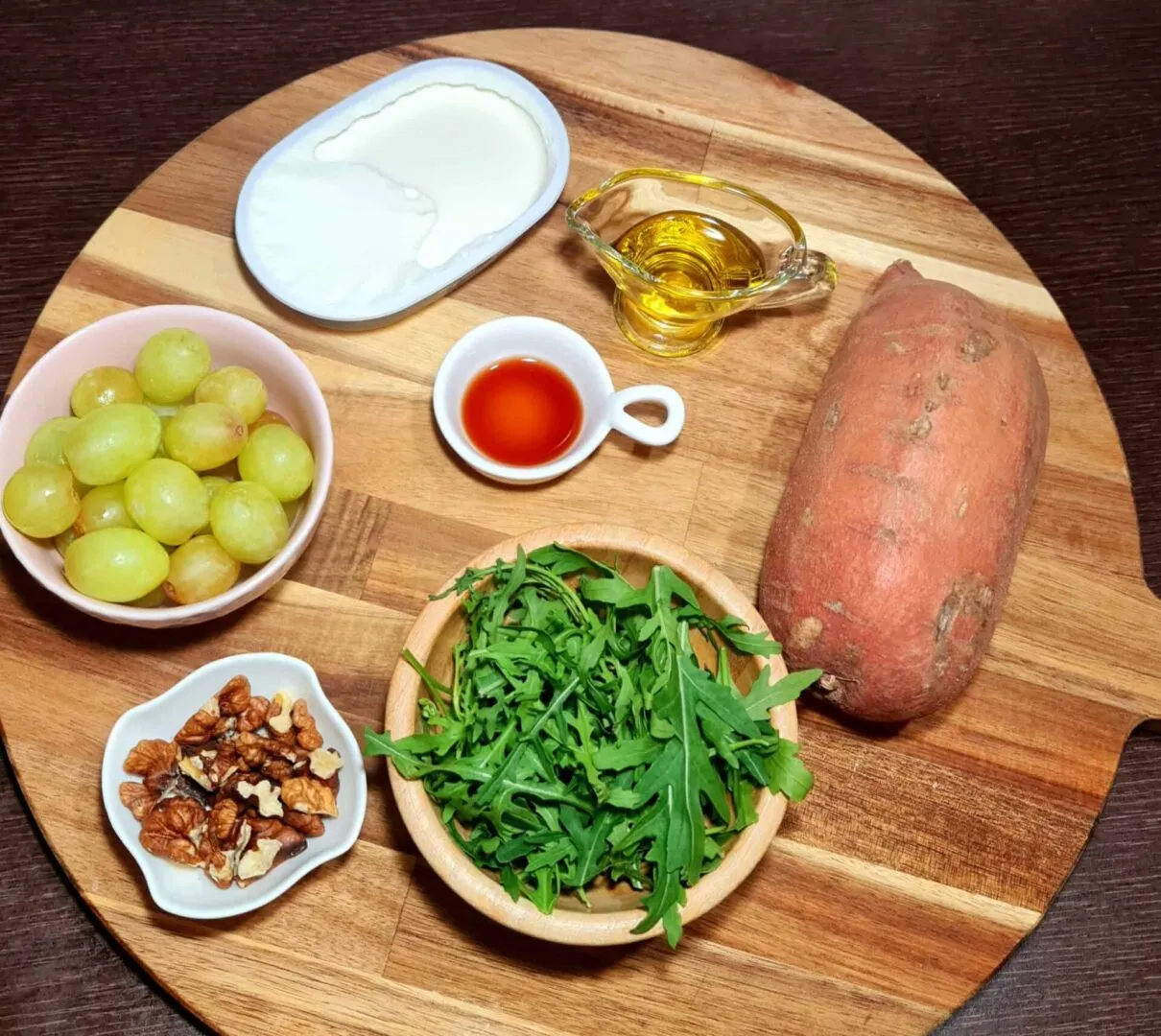 Wooden board with raw sweet potato, green grapes, arugula, walnuts, vegan yogurt, maple syrup and olive oil.