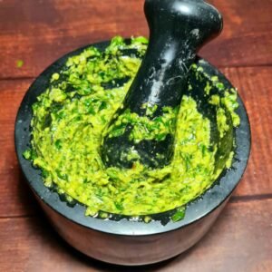 Stone mortar filled with bright green pesto and pestle inside after grinding basil and nuts.