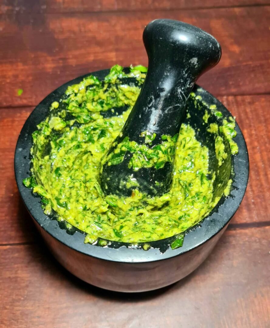 Stone mortar filled with bright green pesto and pestle inside after grinding basil and nuts.