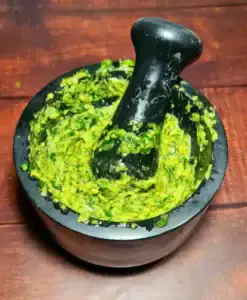 Stone mortar filled with bright green pesto and pestle inside after grinding basil and nuts.