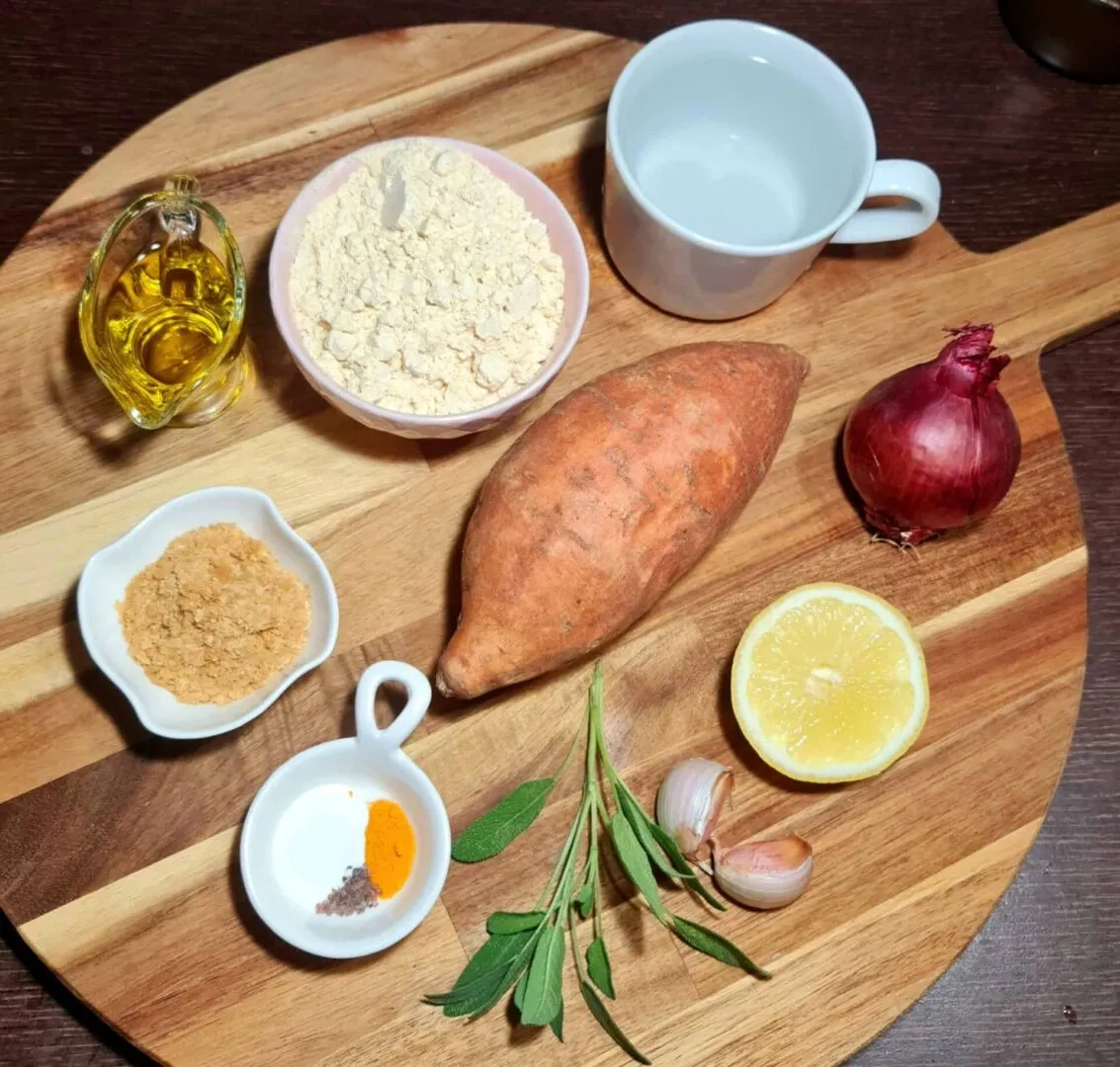 Wooden board with sweet potato, chickpea flour, olive oil, red onion, lemon, garlic, sage, and seasonings for a sweet potato frittata.
