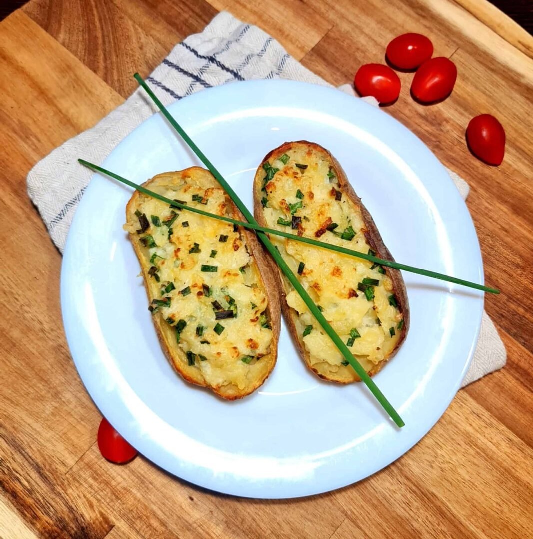Plate with two 2-Ingredient Creamy Stuffed Potatoes crossed by fresh chive sprigs.