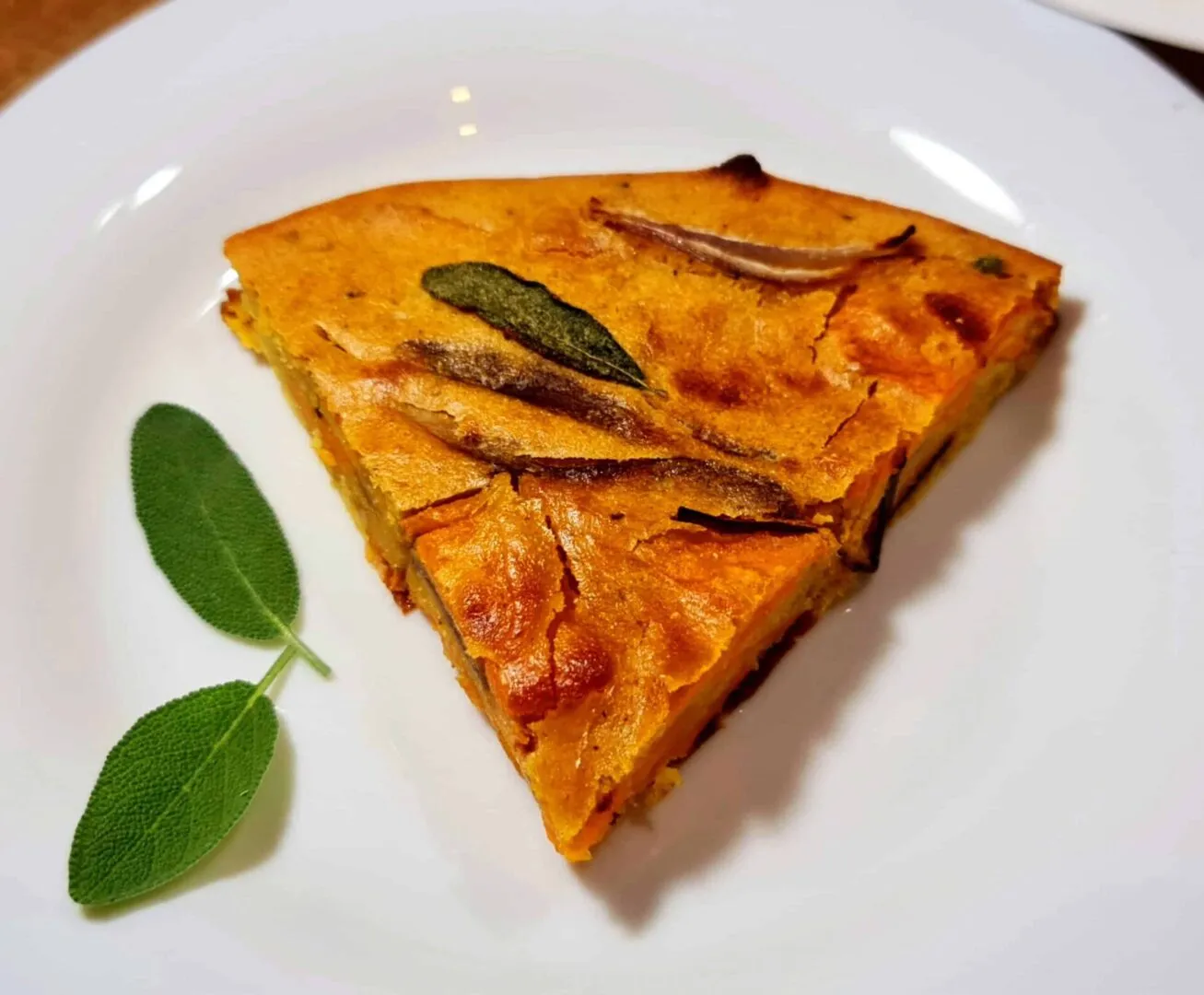 Triangular slice of sweet potato frittata on white plate, garnished with fresh sage leaves.