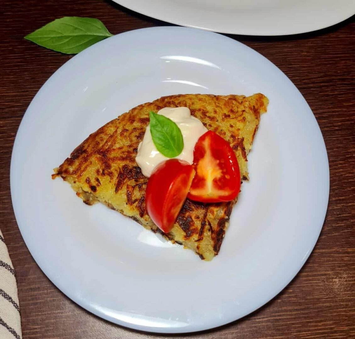 Slice of Crispy 2-Ingredient Potato and Onion Cake garnished with tomato and basil.